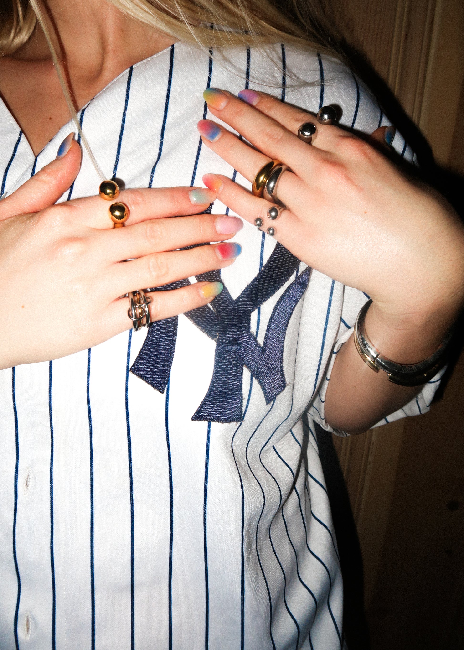 Close-up of hands with multiple rings and nail polish, wearing a striped shirt.
